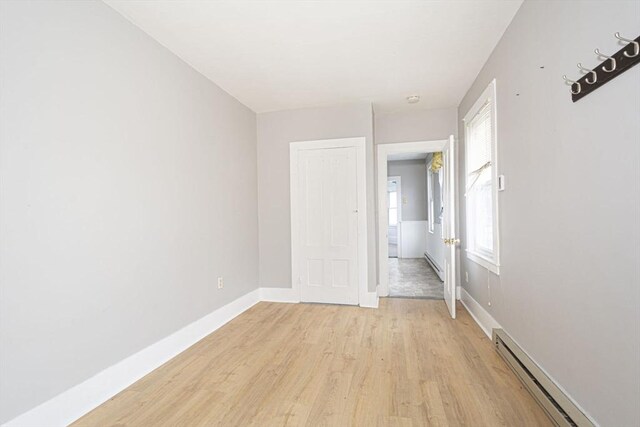 unfurnished bedroom with light wood-style floors, baseboards, a baseboard heating unit, and baseboard heating