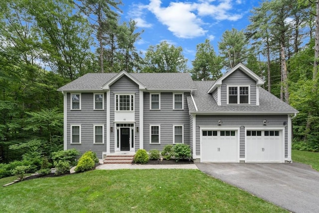 colonial home featuring an attached garage, a shingled roof, a front yard, and aphalt driveway