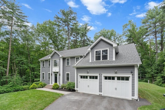 colonial house featuring driveway, an attached garage, a front lawn, and roof with shingles