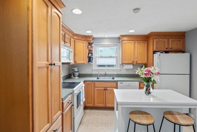 kitchen featuring a breakfast bar, recessed lighting, light countertops, a sink, and white appliances