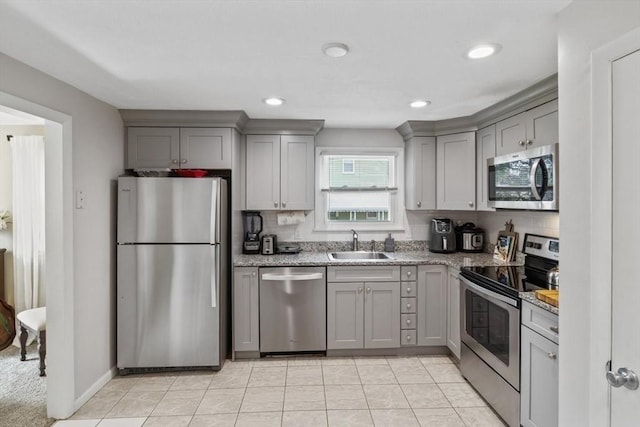 kitchen featuring light stone countertops, gray cabinetry, a sink, appliances with stainless steel finishes, and decorative backsplash