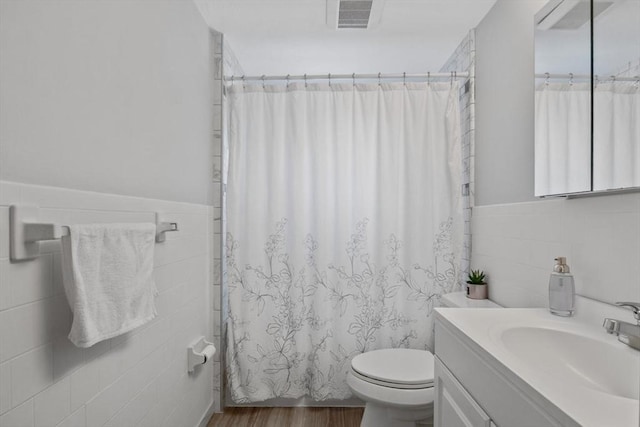 bathroom featuring tile walls, visible vents, toilet, vanity, and wood finished floors