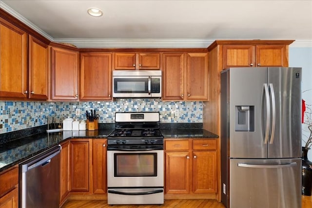 kitchen featuring crown molding, dark stone counters, brown cabinetry, and stainless steel appliances