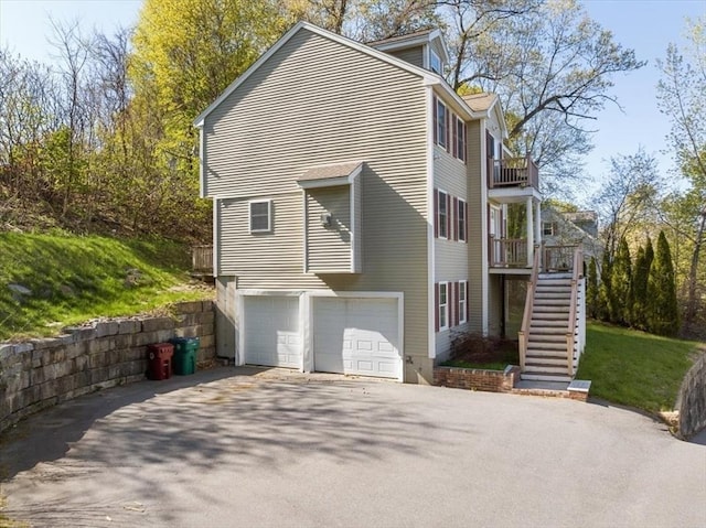 view of side of home featuring stairway, an attached garage, driveway, and a balcony