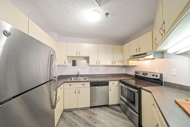 kitchen with appliances with stainless steel finishes, cream cabinets, dark countertops, and under cabinet range hood