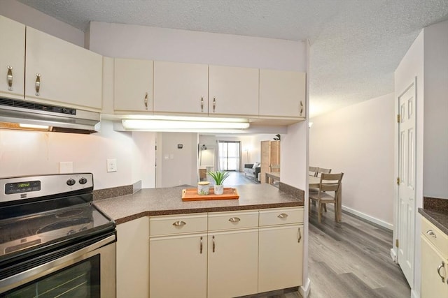 kitchen featuring a textured ceiling, under cabinet range hood, cream cabinetry, dark countertops, and stainless steel range with electric stovetop