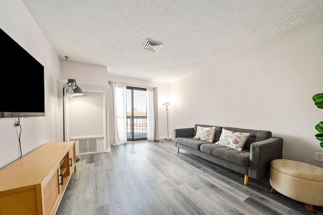 living area with a textured ceiling, wood finished floors, and visible vents