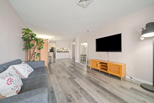 living area with visible vents, a textured ceiling, baseboards, and wood finished floors