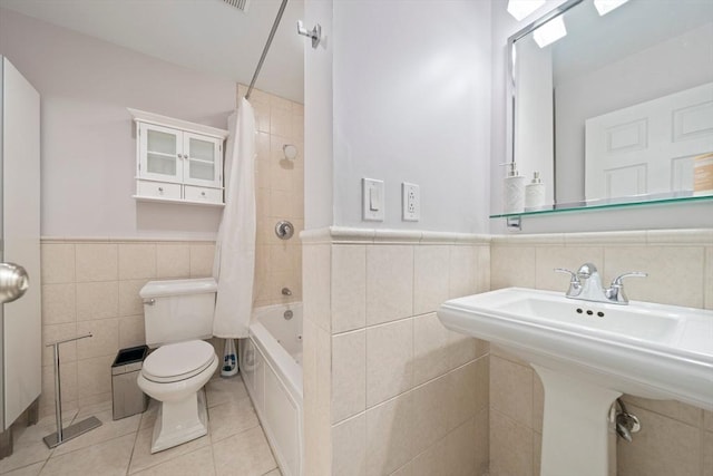 full bath featuring wainscoting, toilet, tile patterned floors, shower / bath combo with shower curtain, and tile walls