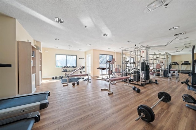 exercise room featuring light wood-type flooring, visible vents, a textured ceiling, and baseboards