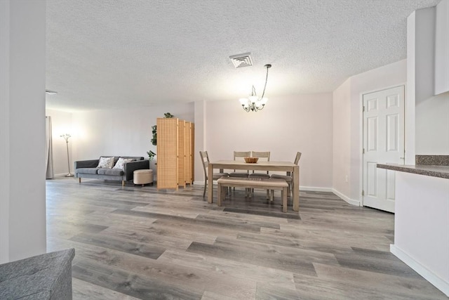 dining space featuring a chandelier, a textured ceiling, wood finished floors, visible vents, and baseboards