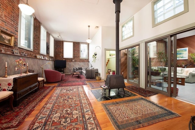 interior space with brick wall, hardwood / wood-style floors, a wood stove, and a high ceiling