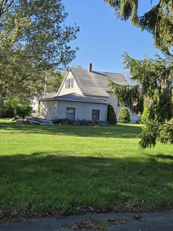 view of property exterior with stucco siding, a chimney, and a yard