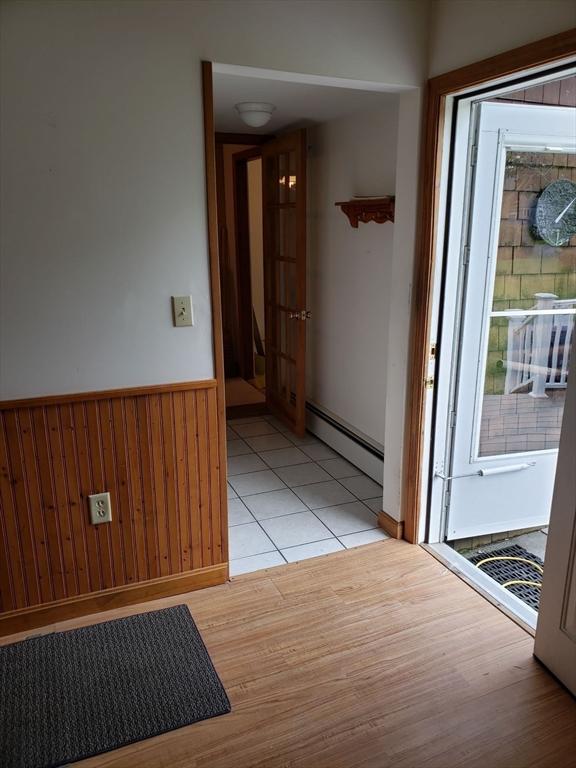 empty room featuring a baseboard radiator, wainscoting, light wood finished floors, baseboards, and wood walls