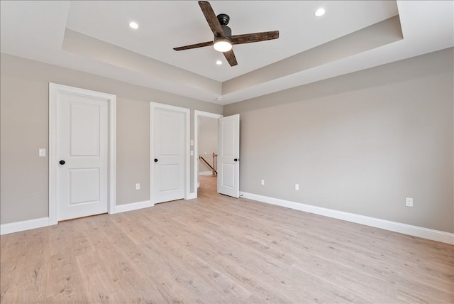 unfurnished bedroom with ceiling fan, light hardwood / wood-style flooring, and a tray ceiling