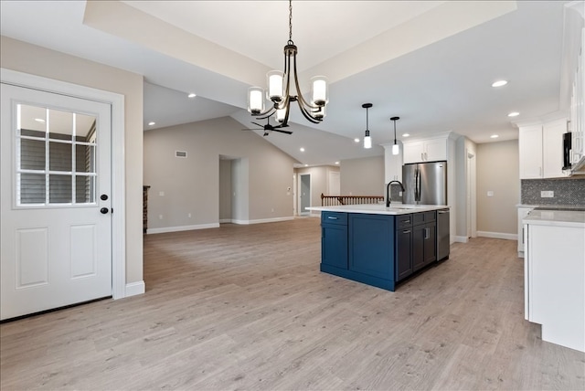 kitchen with hanging light fixtures, white cabinets, appliances with stainless steel finishes, light hardwood / wood-style flooring, and backsplash