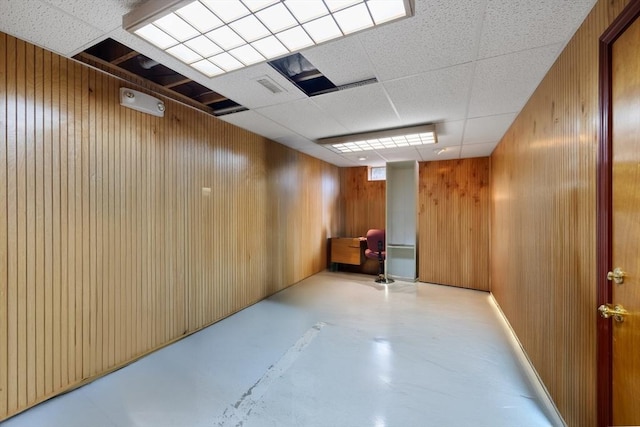 spare room with finished concrete floors, a paneled ceiling, and wood walls