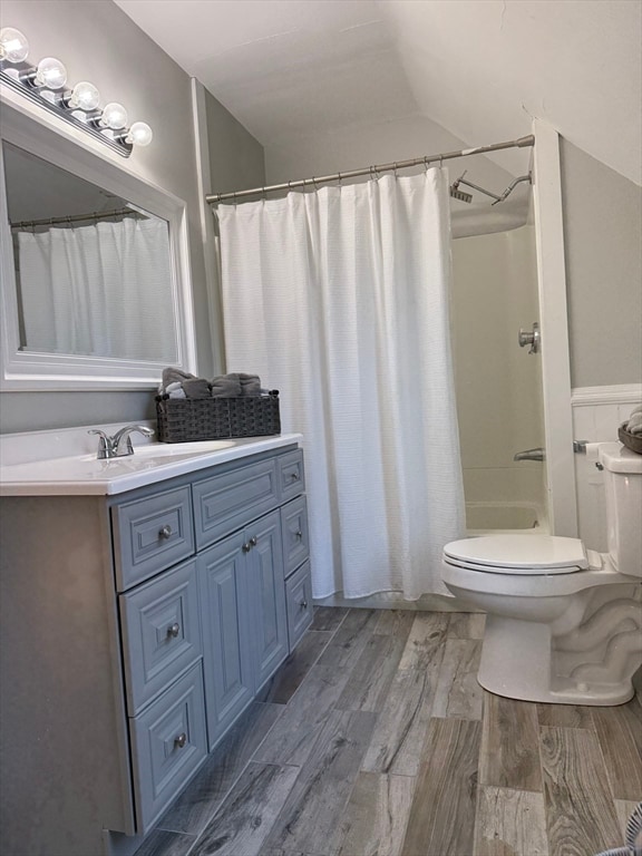 bathroom featuring curtained shower, wood-type flooring, vaulted ceiling, toilet, and vanity