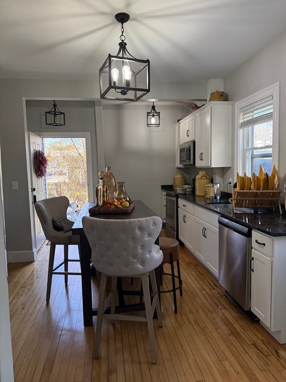 kitchen featuring light wood-type flooring, stainless steel appliances, decorative light fixtures, a notable chandelier, and white cabinetry