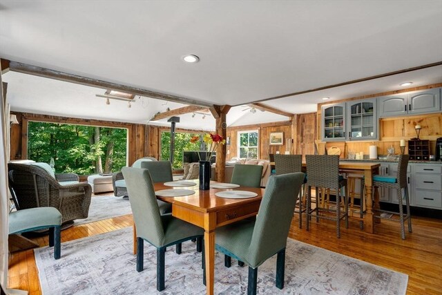 dining room with wooden walls, light hardwood / wood-style floors, and beamed ceiling