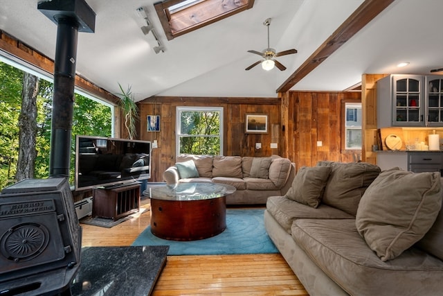 living room with lofted ceiling with skylight, light hardwood / wood-style flooring, a wood stove, ceiling fan, and a baseboard heating unit