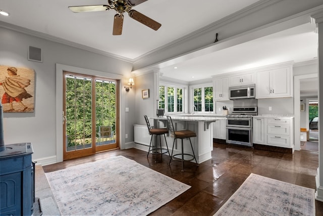 kitchen featuring white cabinets, appliances with stainless steel finishes, light stone counters, ceiling fan, and a kitchen bar