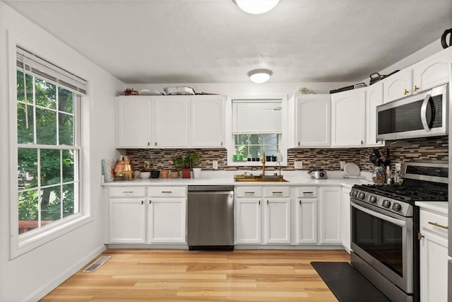 15 N St Unit 2, Haverhill, MA 01830 - kitchen with appliances with stainless steel finishes, backsplash, white cabinetry, light wood-type flooring, and light countertops