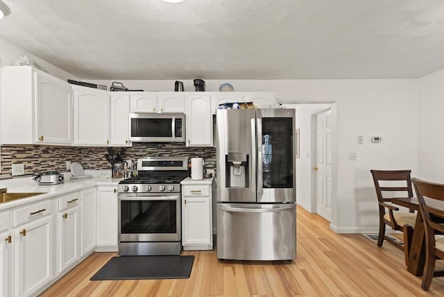 15 N St Unit 2, Haverhill, MA 01830 - kitchen featuring appliances with stainless steel finishes, light wood-style floors, decorative backsplash, light countertops, and white cabinets