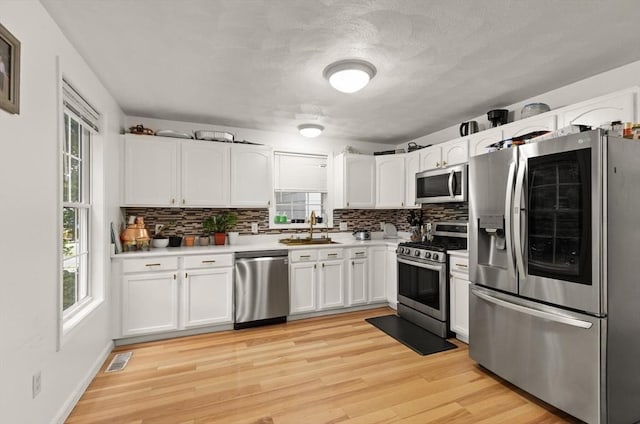 15 N St Unit 2, Haverhill, MA 01830 - kitchen featuring stainless steel appliances, decorative backsplash, white cabinetry, healthy amount of natural light, and a textured ceiling