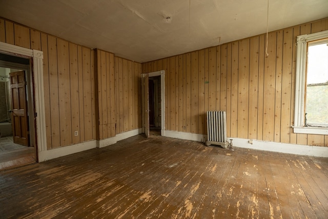 empty room with dark wood-type flooring, radiator, and wood walls