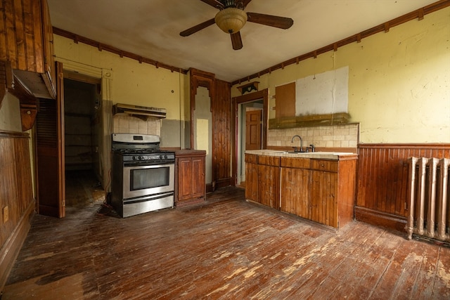 kitchen featuring dark wood-type flooring, backsplash, stainless steel gas range oven, and radiator