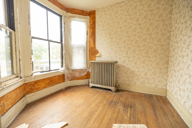 unfurnished room with hardwood / wood-style floors, radiator heating unit, and a healthy amount of sunlight