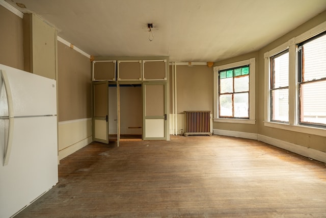 unfurnished bedroom featuring hardwood / wood-style flooring, white refrigerator, and radiator heating unit