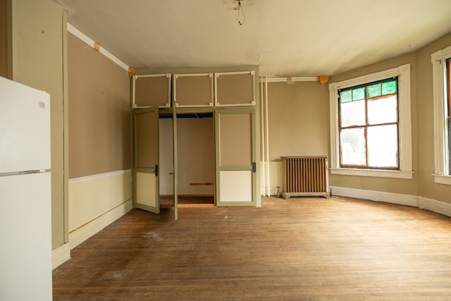 unfurnished bedroom with white refrigerator, wood-type flooring, and radiator