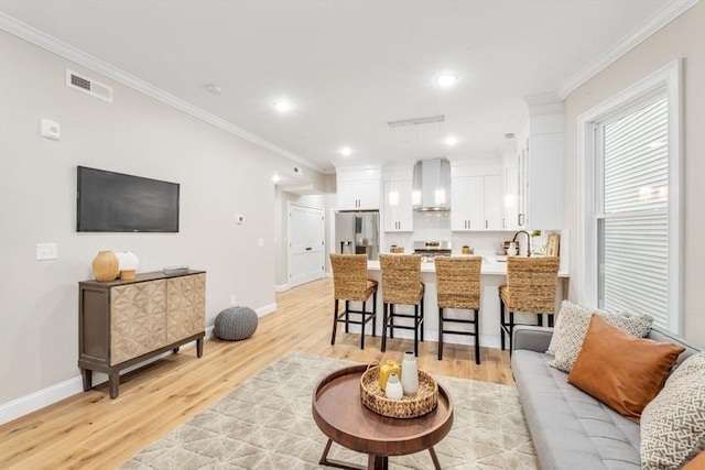 living room featuring crown molding, sink, and light hardwood / wood-style floors