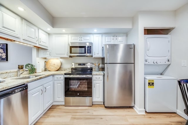 kitchen featuring light wood-type flooring, stainless steel appliances, sink, white cabinetry, and stacked washer / drying machine