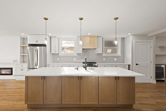 kitchen featuring beverage cooler, appliances with stainless steel finishes, an island with sink, light stone counters, and white cabinets