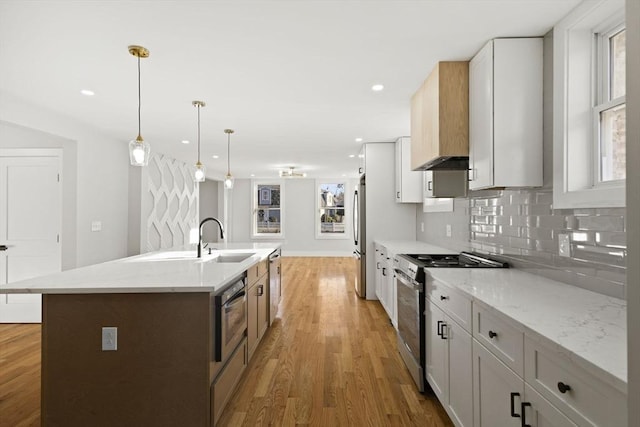 kitchen with stainless steel appliances, white cabinets, decorative light fixtures, light stone countertops, and a center island with sink