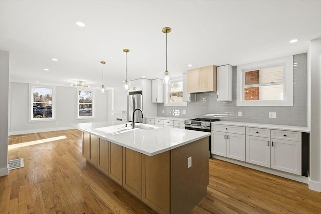 kitchen featuring decorative light fixtures, a center island with sink, tasteful backsplash, light wood-type flooring, and white cabinetry