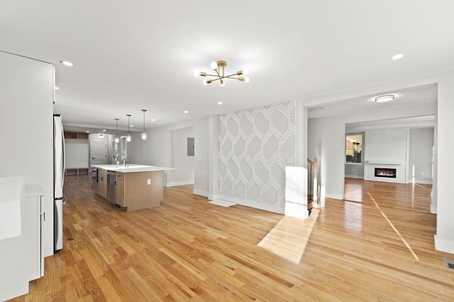 unfurnished living room featuring electric panel, light wood-type flooring, a chandelier, and sink