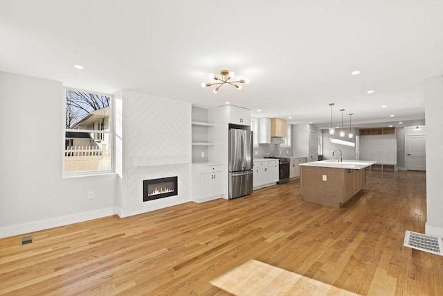 kitchen featuring decorative light fixtures, an island with sink, stainless steel appliances, light wood-type flooring, and white cabinetry