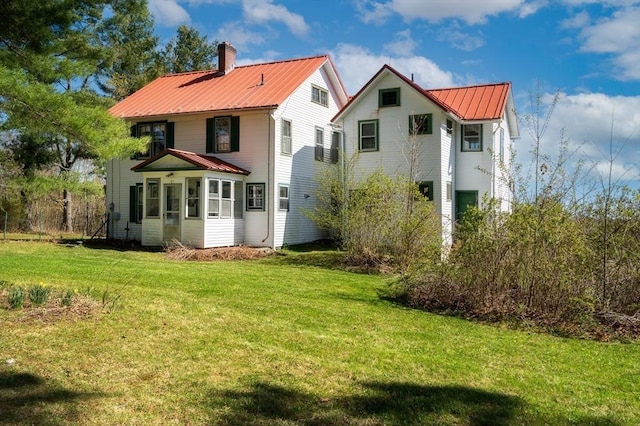 rear view of house with a lawn, a chimney, and metal roof