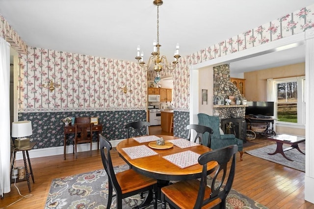 dining area featuring a fireplace, light wood-style flooring, a notable chandelier, and wallpapered walls