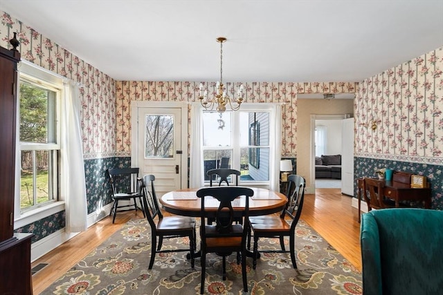 dining space featuring wood finished floors, wallpapered walls, a notable chandelier, visible vents, and wainscoting