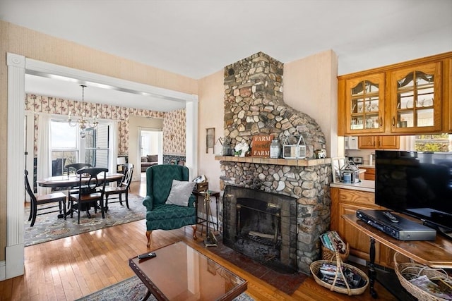 living area with a stone fireplace, a notable chandelier, wood-type flooring, and wallpapered walls