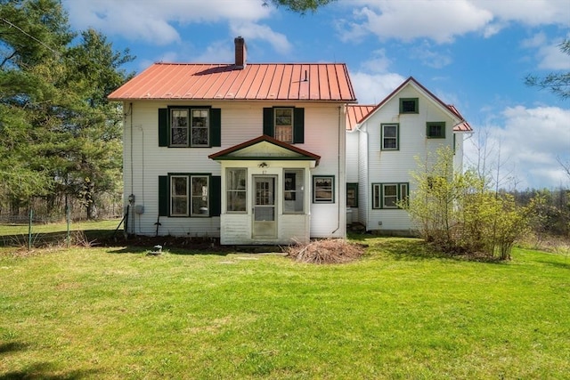 rear view of property featuring metal roof, a chimney, a lawn, and a standing seam roof