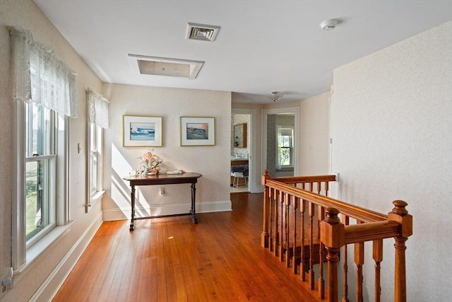 hallway with hardwood / wood-style flooring, baseboards, an upstairs landing, and visible vents