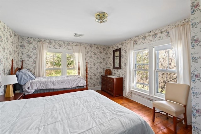 bedroom with visible vents, baseboards, wallpapered walls, and wood finished floors
