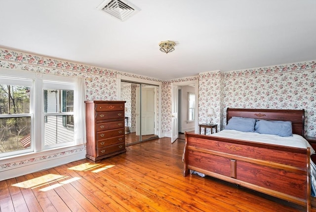 bedroom featuring multiple windows, light wood-style floors, visible vents, and wallpapered walls