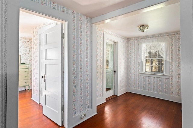 corridor with wallpapered walls, wood finished floors, and baseboards